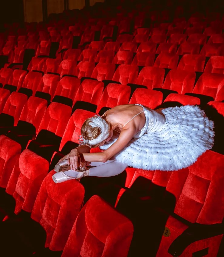 Bailarina de ballet clásico estirando en las butacas de un teatro vacío